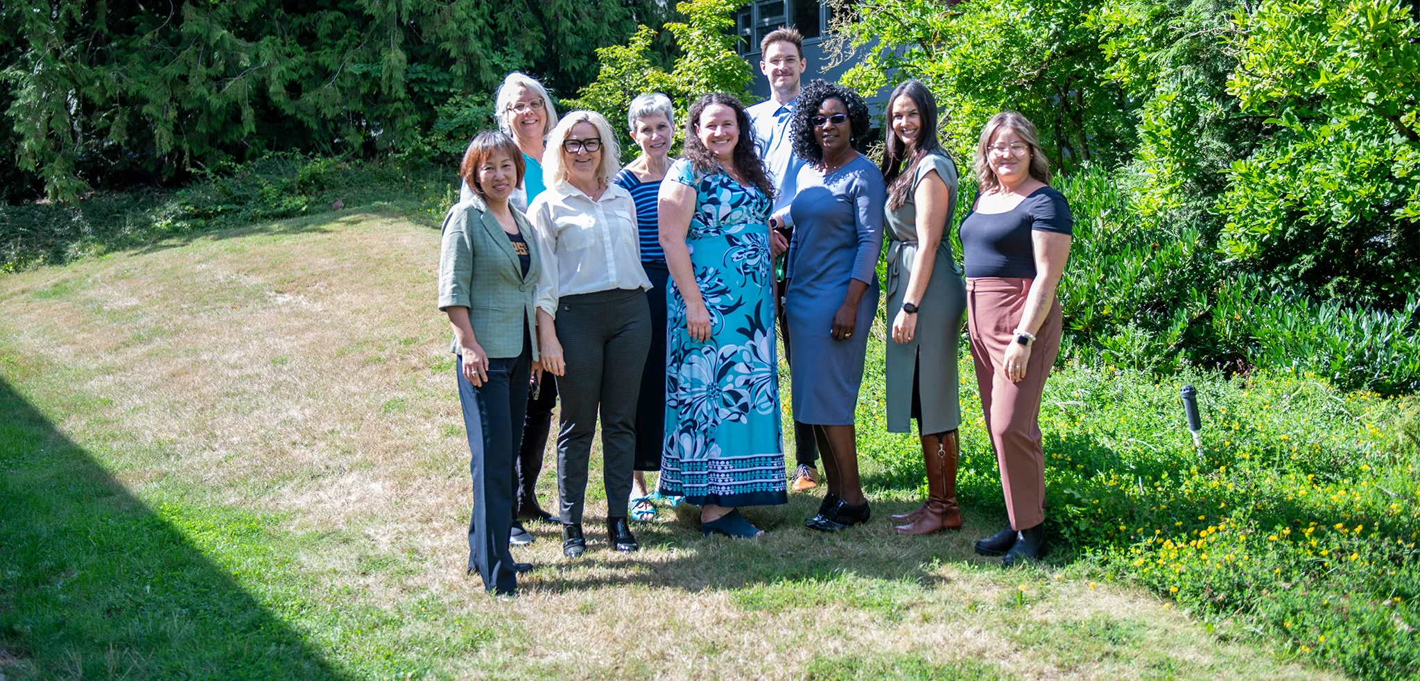 The Relationship and Fund Development team standing outside on a grassy area, posing for a photo with trees and a building in the background.