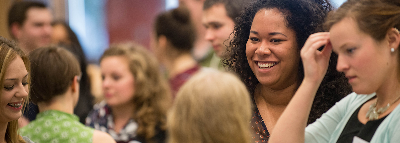 A group of people socializing at an indoor event, with several individuals engaged in conversation and smiling.