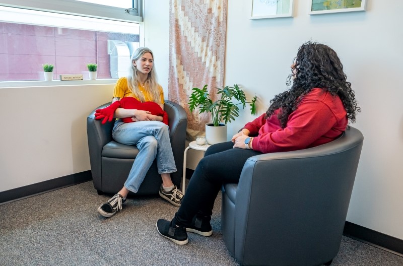 A student and staff member sit across from one another in comfy armchairs at the UFV Wellness Centre.