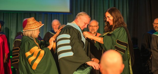A ceremonial installation at UFV where faculty members place academic regalia on the university president during an October ceremony.