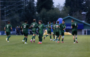 UFV Cascades soccer players in green uniforms gather on the field, exchanging high-fives and celebrating during a match.